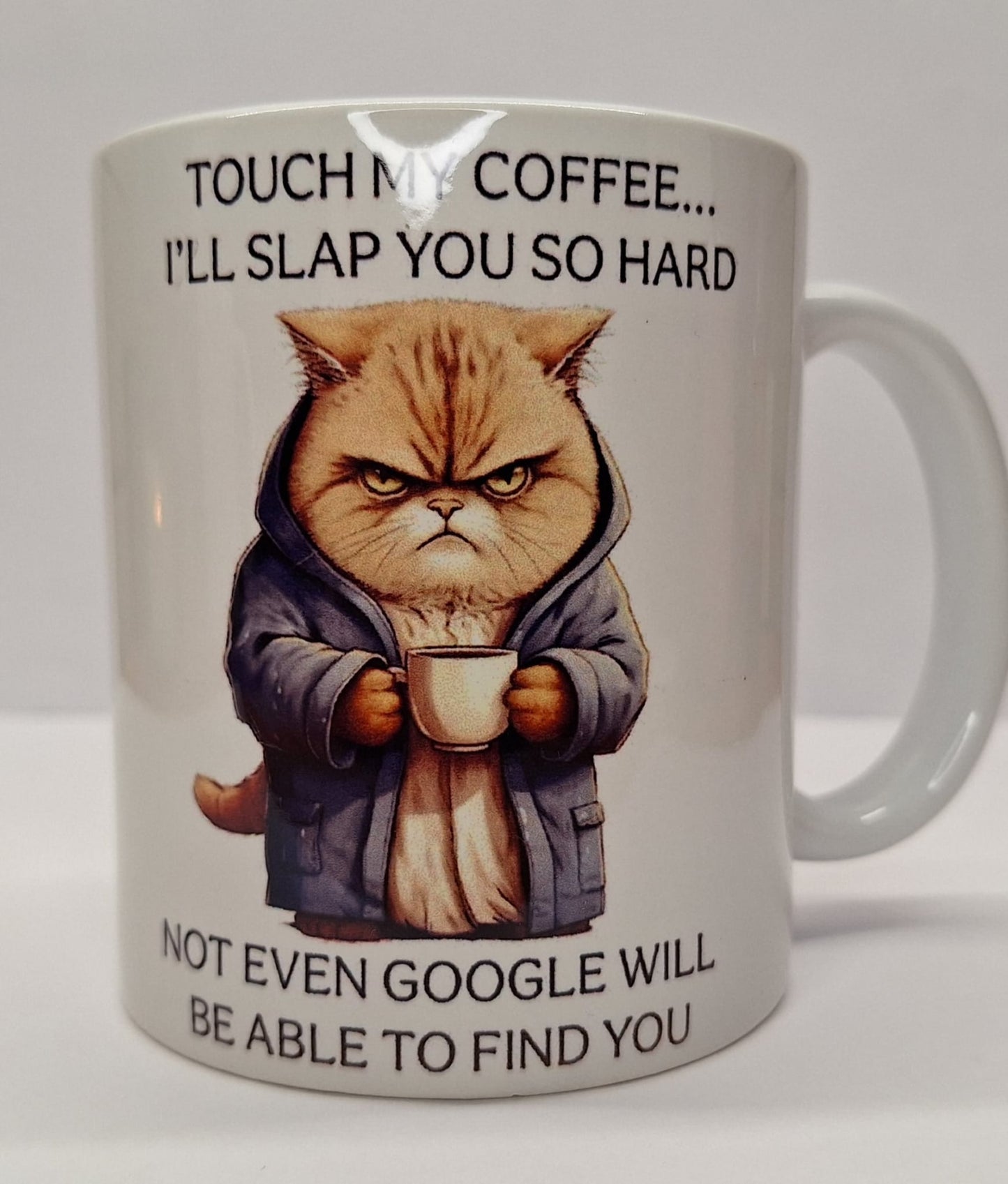 Weiße Tasse mit wütender Katze im Mantel, hält eine Kaffeetasse in den Pfoten, witziger Spruch: „Touch my coffee... I’ll slap you so hard…“
