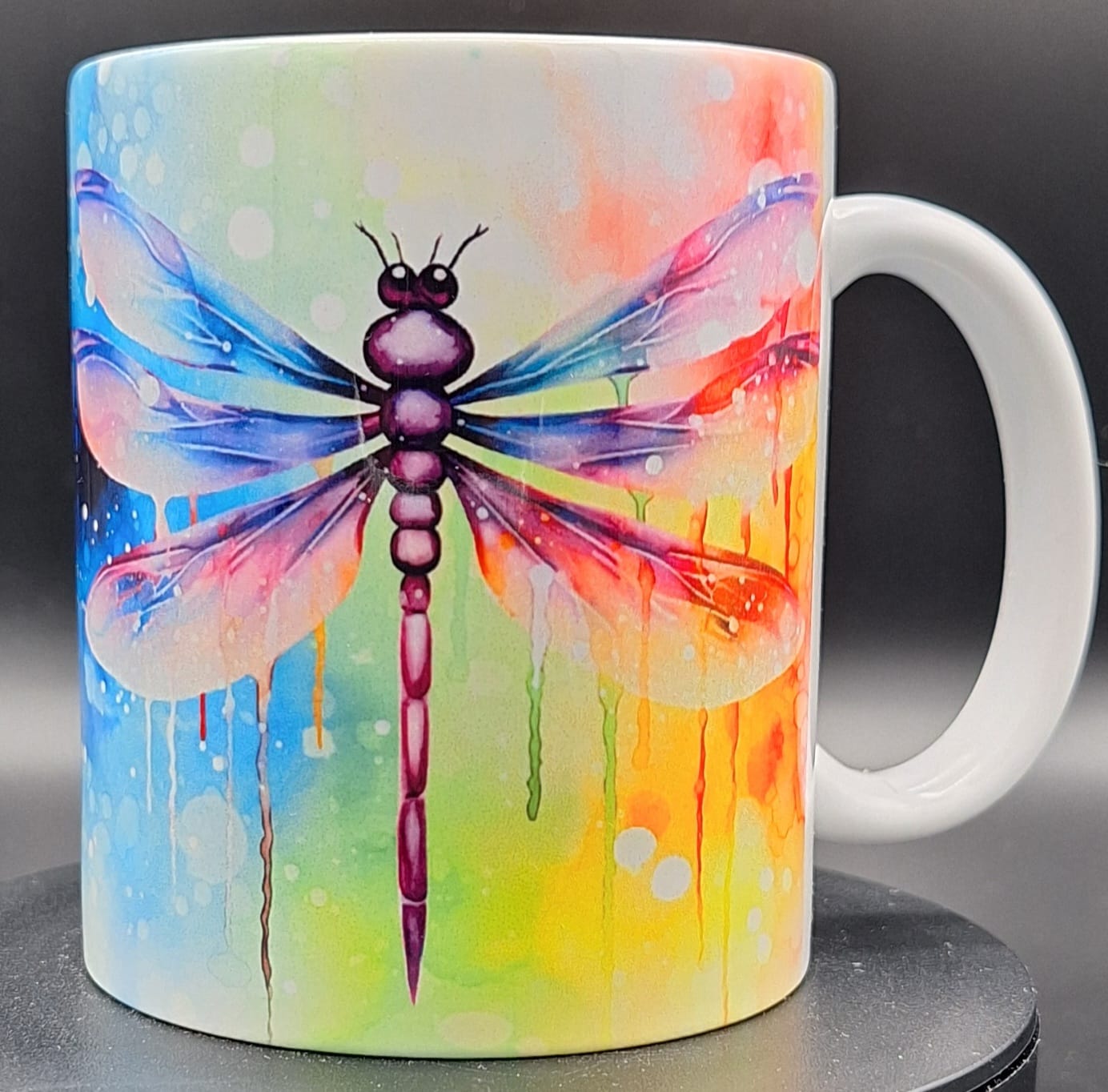 Weiße Tasse mit bunter Libelle im Aquarellstil, Flügel in Regenbogenfarben mit Farbverlauf und Watercolor-Effekt auf hellem Hintergrund